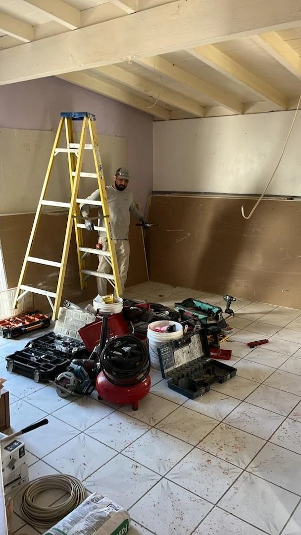 A builder on a yellow ladder preparing a room for drywall and electrical updates in Anaheim Hills.