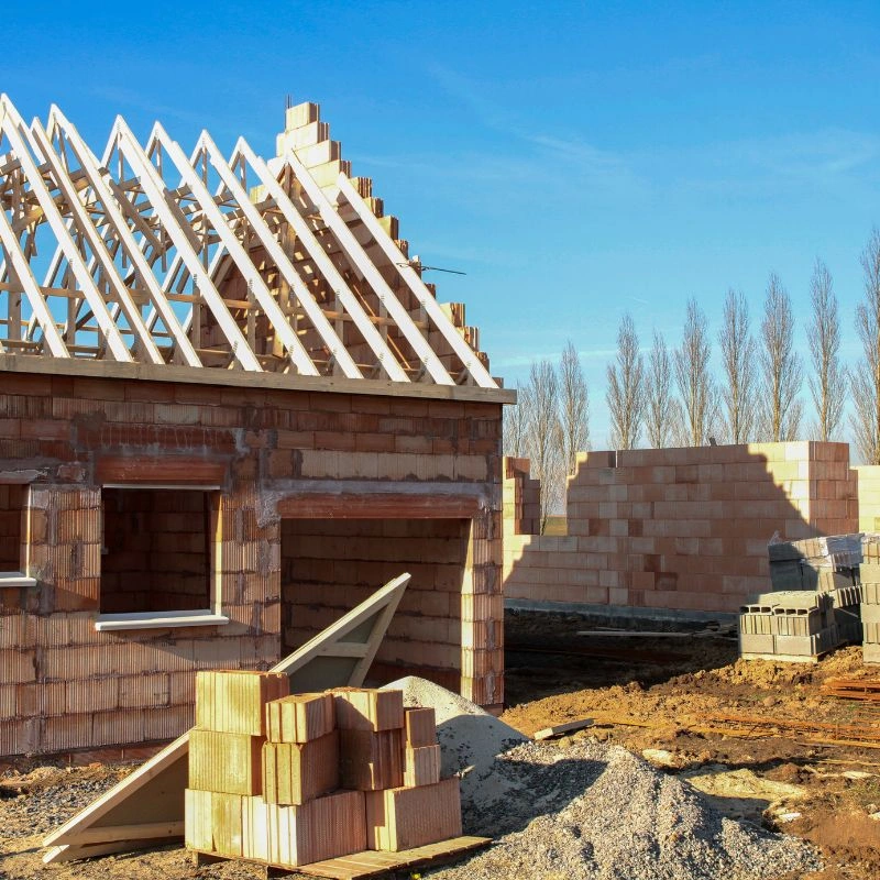A residential building under construction showing unpainted brick walls and wood roof trusses in Fullerton.