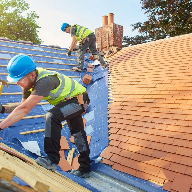 Two construction tradesmen in safety vests hand-laying terracotta clay roof tiles near a valley in Brea.