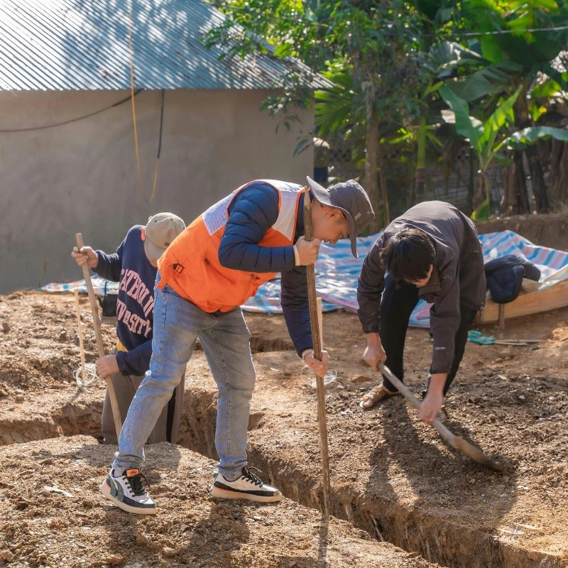 Three workers digging deep structural drainage trenches in a dirt yard with shovels in Fullerton.