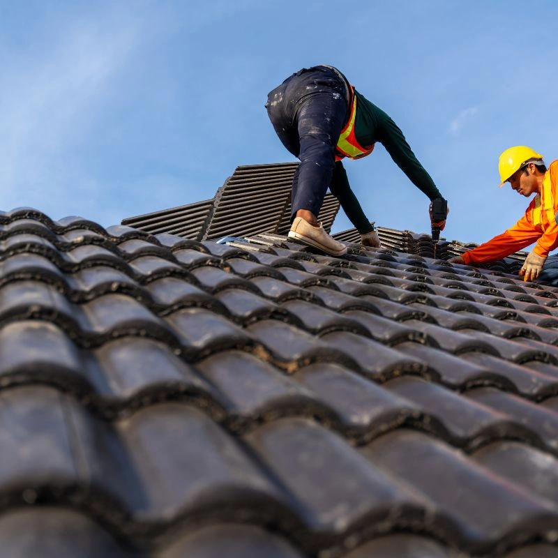 A roofer in safety gear leaning down to screw dark concrete interlocking slates into timber roof battens in Fullerton.