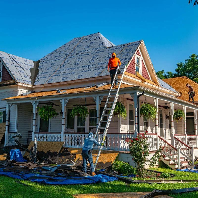 A roofer on a tall extension ladder applying a synthetic water barrier membrane to a house in Anaheim Hills.
