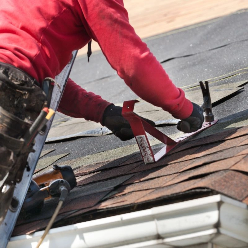 A roofer in a red sweatshirt using a hammer and a shingle removal tool on an asphalt shingle roof in Yorba Linda.