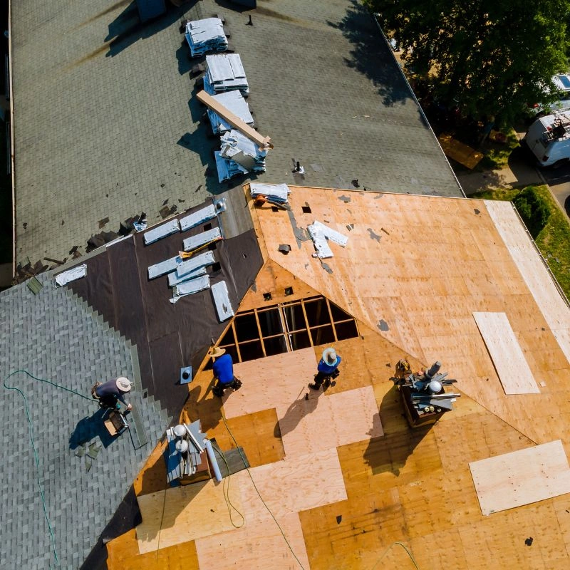 An aerial drone view of roofers stripping asphalt shingles down to raw plywood decking in Yorba Linda.