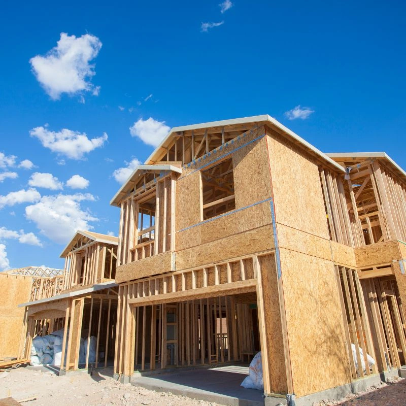 Row of multi story residential house frames sheathed in brown plywood under a bright blue sky in Brea.