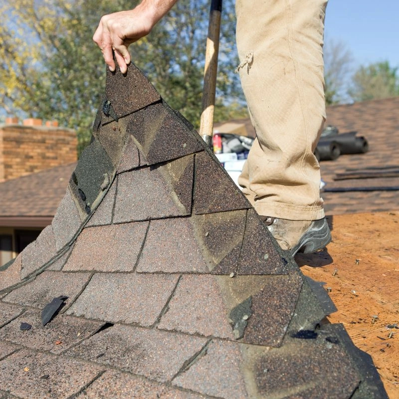 Close shot of a worker lifting a massive strip of old interlocking shingles using a steel tear-off shovel in Tustin.