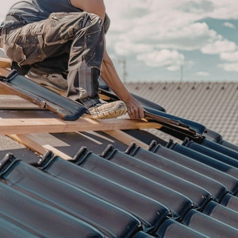 Close view of a worker placing shiny dark glazed clay tiles onto raw timber framing lines during a project in Tustin.